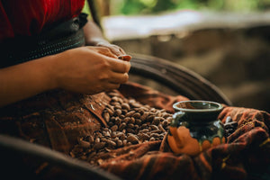 Collective member hand-peeling cacao beans beside a ceramic cup